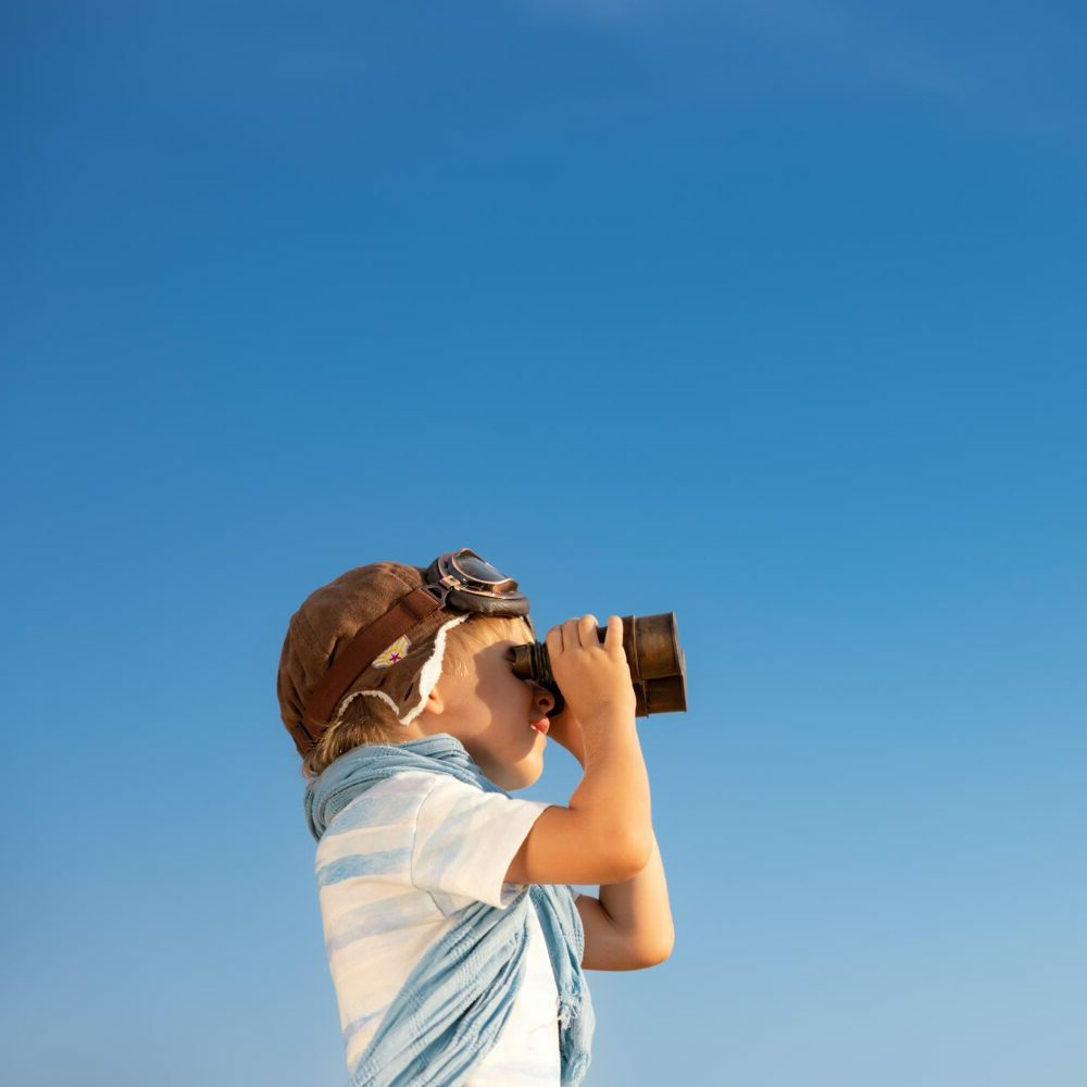 child-looking-through-binoculars-against-blue-sky-kid-having-fun-outdoor-summer-adventure-travel-concept